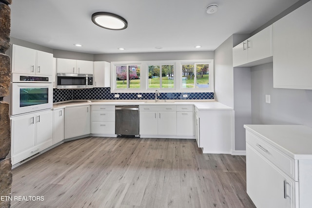 kitchen with tasteful backsplash, appliances with stainless steel finishes, sink, white cabinetry, and light hardwood / wood-style floors