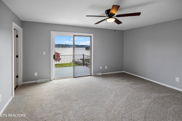 unfurnished room featuring a water view, carpet floors, and ceiling fan