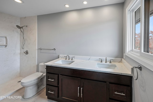 bathroom with toilet, vanity, a tile shower, and tile patterned flooring