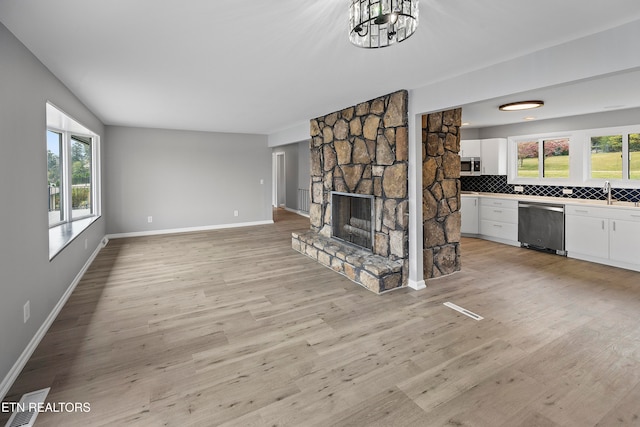 unfurnished living room with a chandelier, a stone fireplace, and light wood-type flooring