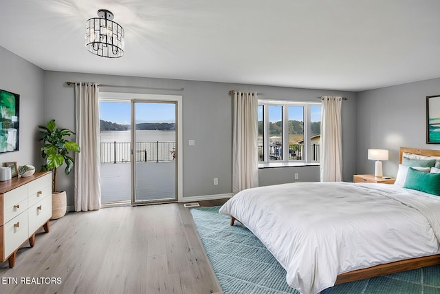 bedroom featuring an inviting chandelier, access to exterior, multiple windows, and light wood-type flooring