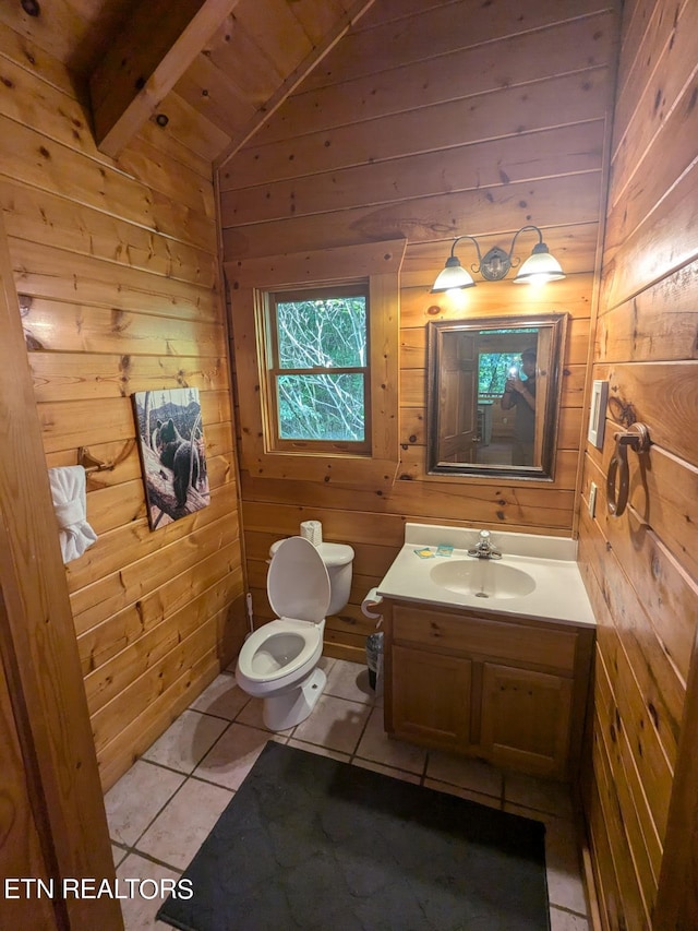 bathroom featuring lofted ceiling with beams, wood walls, vanity, toilet, and tile patterned floors