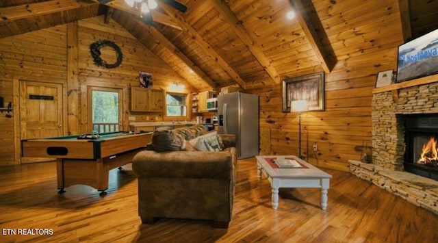 living room featuring pool table, light hardwood / wood-style floors, wooden walls, a stone fireplace, and ceiling fan