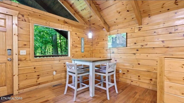 dining area with vaulted ceiling with beams, hardwood / wood-style flooring, wooden walls, and wooden ceiling