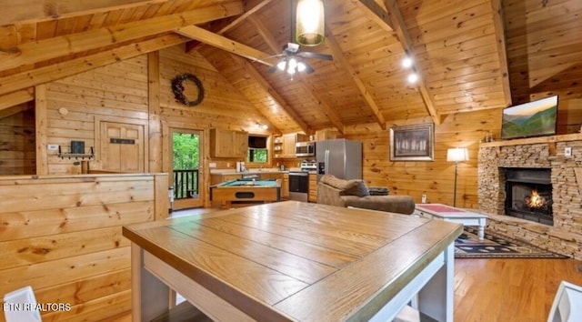 kitchen with ceiling fan, a stone fireplace, wooden walls, appliances with stainless steel finishes, and light wood-type flooring