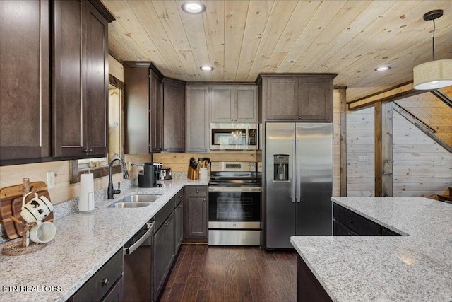 kitchen featuring dark wood-type flooring, sink, stainless steel appliances, decorative light fixtures, and light stone countertops