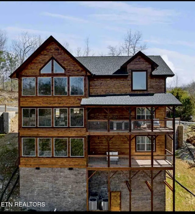 rear view of house with central AC unit and roof with shingles