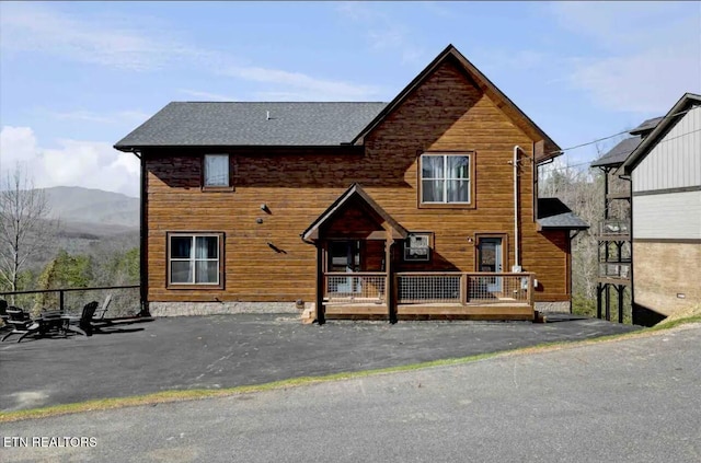 back of property with a mountain view and a shingled roof