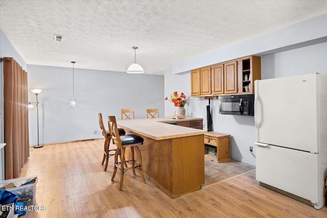 kitchen with kitchen peninsula, light hardwood / wood-style floors, a textured ceiling, decorative light fixtures, and white fridge