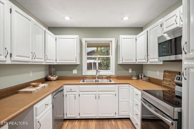 kitchen with white cabinetry, sink, light wood-type flooring, and appliances with stainless steel finishes