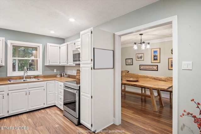 kitchen featuring white cabinets, sink, hanging light fixtures, light wood-type flooring, and stainless steel appliances