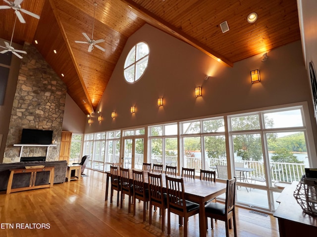 dining area featuring a stone fireplace, wooden ceiling, high vaulted ceiling, light hardwood / wood-style floors, and ceiling fan