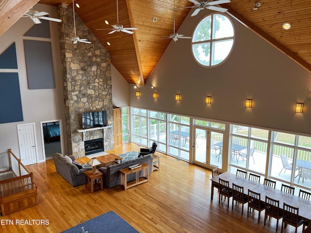 living room with a stone fireplace, wood ceiling, high vaulted ceiling, and light wood-type flooring