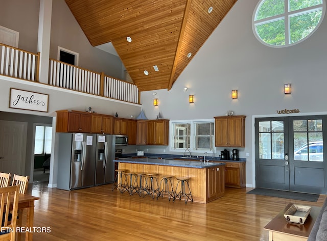 kitchen featuring a kitchen island, a breakfast bar area, light hardwood / wood-style flooring, stainless steel appliances, and high vaulted ceiling