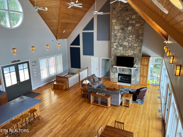 living room featuring a stone fireplace, hardwood / wood-style floors, wooden ceiling, beam ceiling, and high vaulted ceiling