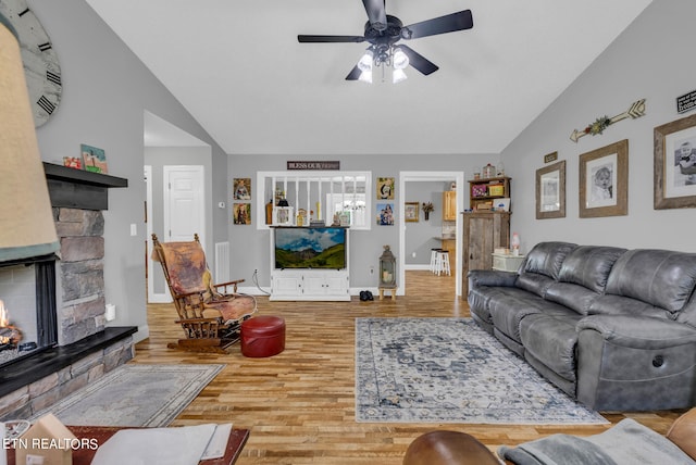 living room with ceiling fan, light hardwood / wood-style floors, a stone fireplace, and lofted ceiling