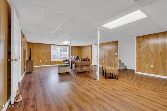 living room featuring a paneled ceiling, wooden walls, and wood-type flooring