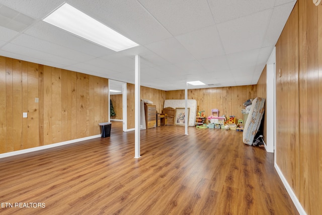 basement featuring a paneled ceiling, wood walls, and hardwood / wood-style flooring