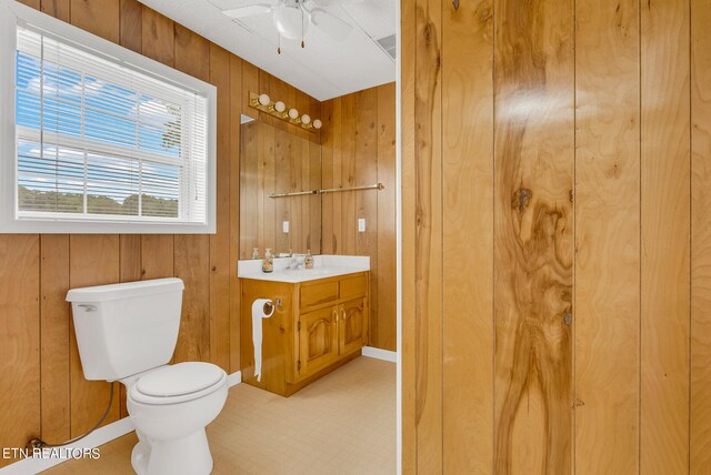 bathroom with ceiling fan, wooden walls, vanity, and toilet