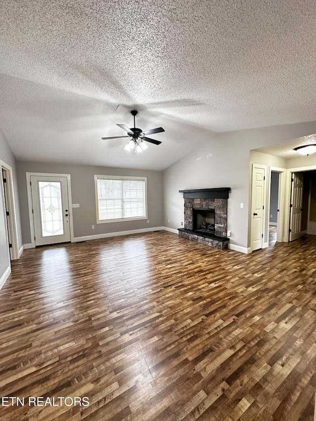 unfurnished living room with a textured ceiling, ceiling fan, dark hardwood / wood-style floors, a stone fireplace, and lofted ceiling