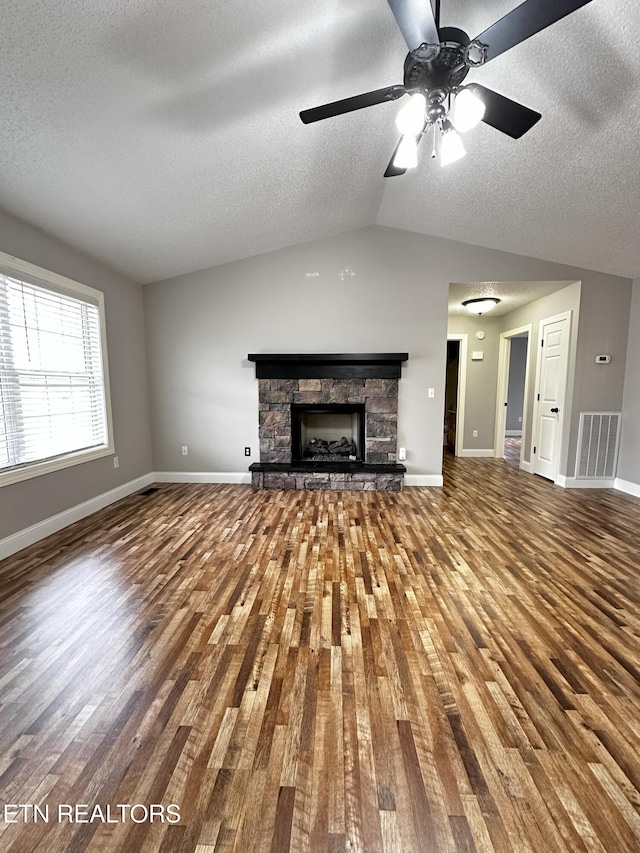 unfurnished living room featuring lofted ceiling, hardwood / wood-style flooring, ceiling fan, a fireplace, and a textured ceiling