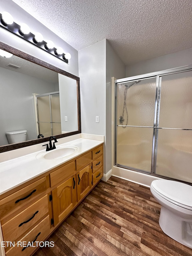 bathroom featuring vanity, a textured ceiling, toilet, and a shower with shower door