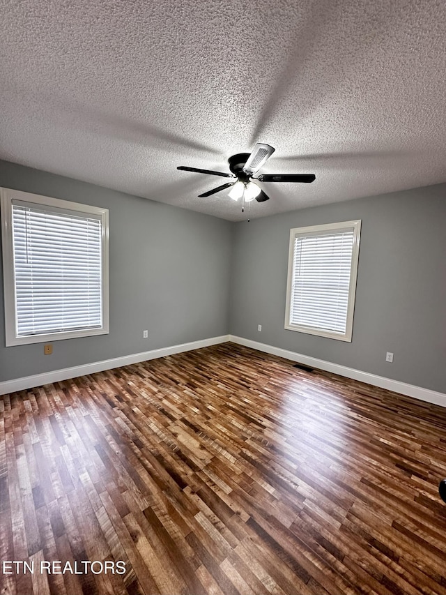 empty room with plenty of natural light, ceiling fan, dark hardwood / wood-style flooring, and a textured ceiling