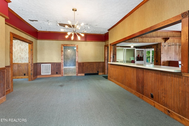 carpeted spare room featuring a notable chandelier, wood walls, and a textured ceiling