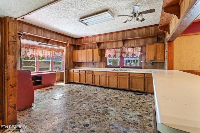 kitchen featuring a textured ceiling, sink, wooden walls, ornamental molding, and ceiling fan