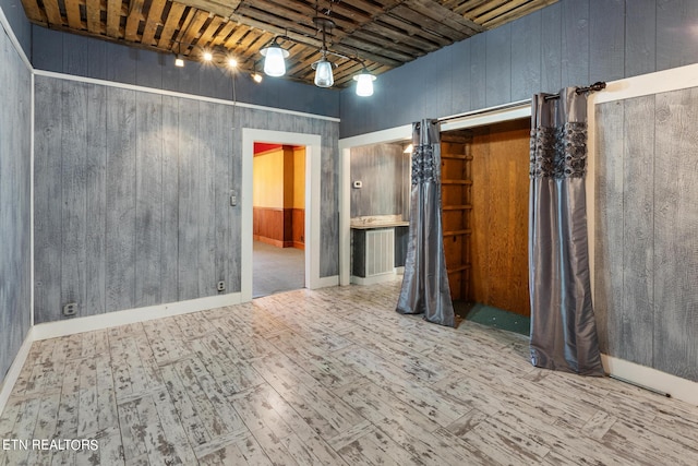 unfurnished room featuring wooden walls, track lighting, a high ceiling, wooden ceiling, and hardwood / wood-style floors