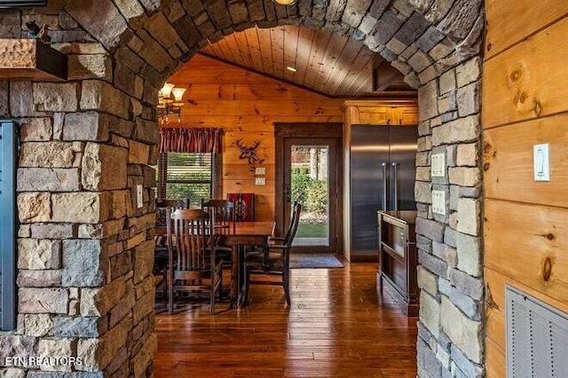 unfurnished dining area featuring lofted ceiling, wood walls, wooden ceiling, and dark wood-type flooring