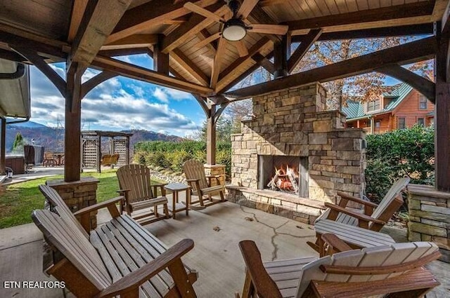 view of patio / terrace featuring an outdoor stone fireplace, ceiling fan, and a gazebo