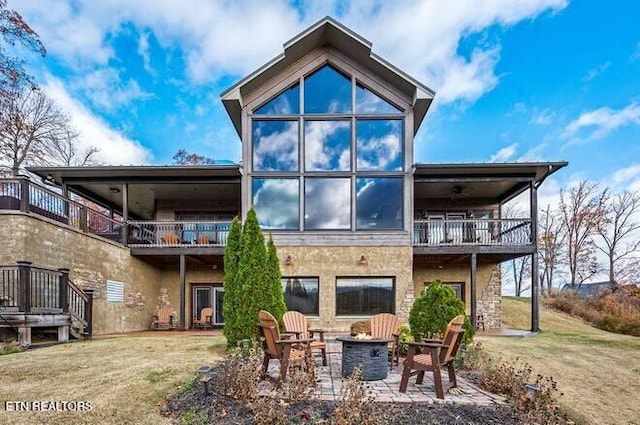 rear view of property featuring a balcony, ceiling fan, a fire pit, a patio area, and a yard