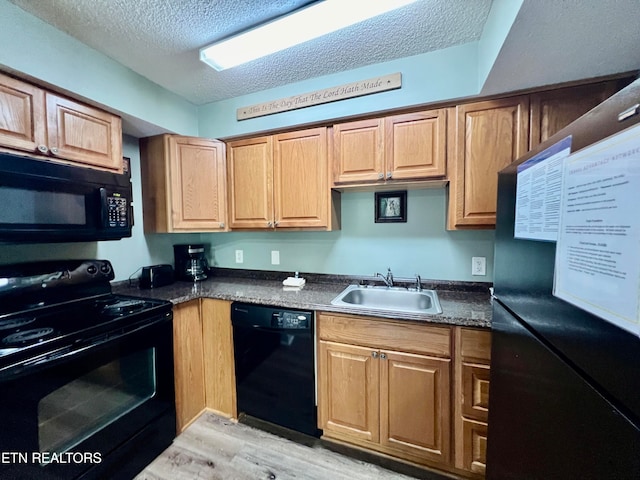 kitchen featuring light wood-type flooring, black appliances, a textured ceiling, dark stone counters, and sink