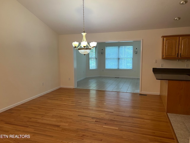 unfurnished dining area with light hardwood / wood-style floors, a notable chandelier, and lofted ceiling