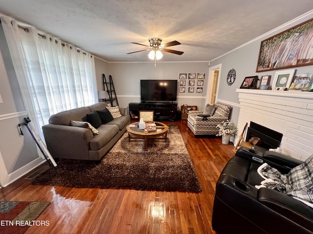 living room featuring a brick fireplace, dark hardwood / wood-style flooring, a textured ceiling, crown molding, and ceiling fan