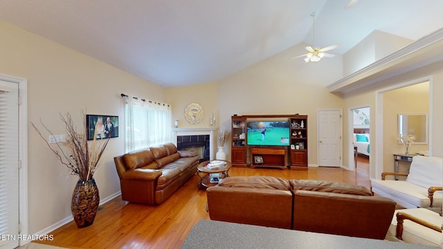 living room featuring ceiling fan, a tiled fireplace, hardwood / wood-style floors, and high vaulted ceiling