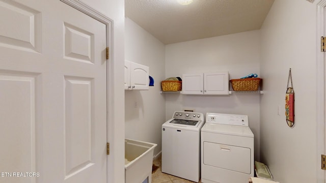 laundry area with light tile patterned floors, a textured ceiling, cabinets, sink, and washer and dryer