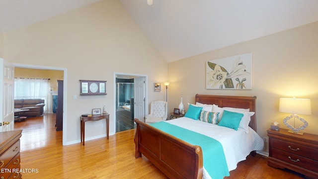 bedroom featuring light wood-type flooring, ensuite bath, and high vaulted ceiling