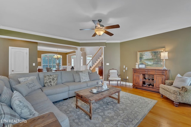 living room featuring ceiling fan with notable chandelier, light hardwood / wood-style flooring, decorative columns, and ornamental molding