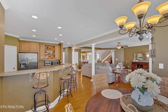 kitchen with a kitchen bar, stainless steel appliances, decorative columns, crown molding, and light hardwood / wood-style floors