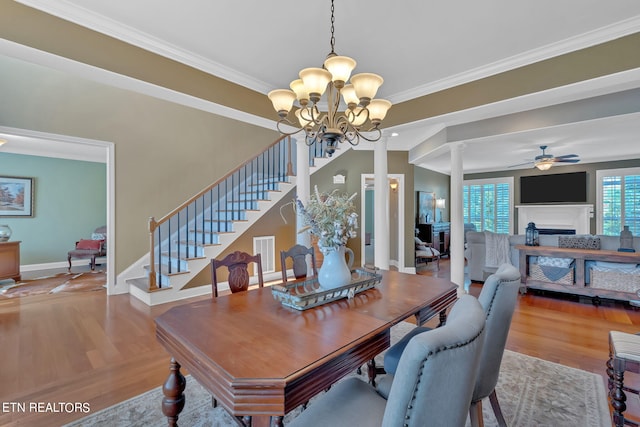 dining space with wood-type flooring, ceiling fan with notable chandelier, decorative columns, and ornamental molding