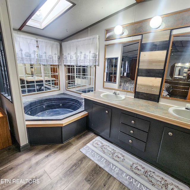 bathroom featuring vanity, vaulted ceiling with skylight, a washtub, and hardwood / wood-style flooring