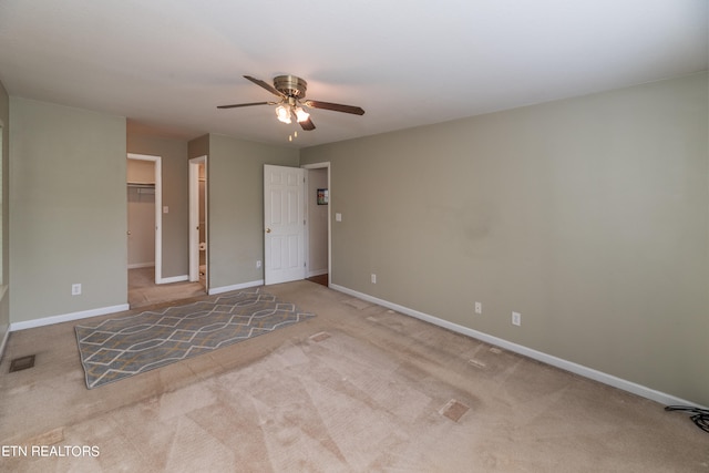 unfurnished bedroom with a spacious closet, ceiling fan, light colored carpet, and a closet