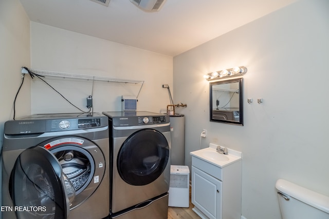 clothes washing area featuring water heater, washing machine and dryer, sink, and light hardwood / wood-style flooring