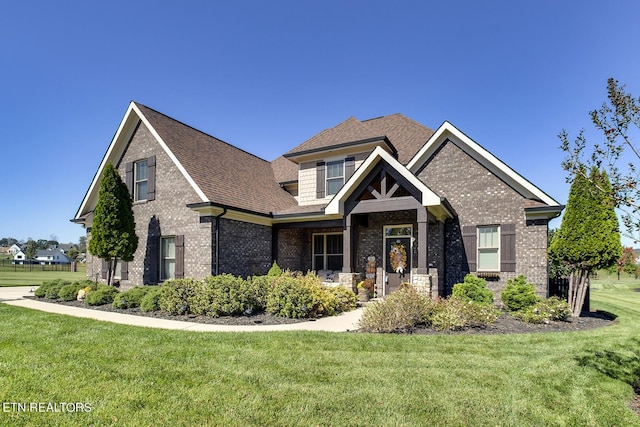 craftsman house with brick siding, a front yard, and roof with shingles