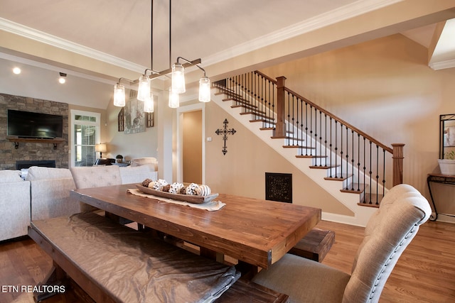 dining room featuring a stone fireplace, crown molding, and hardwood / wood-style floors