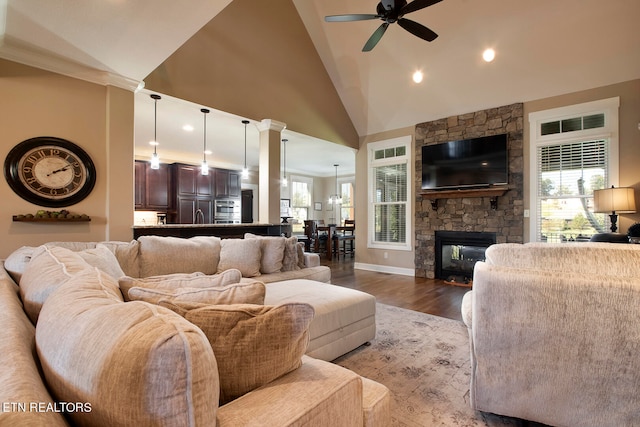 living room with ceiling fan, a stone fireplace, hardwood / wood-style floors, and high vaulted ceiling