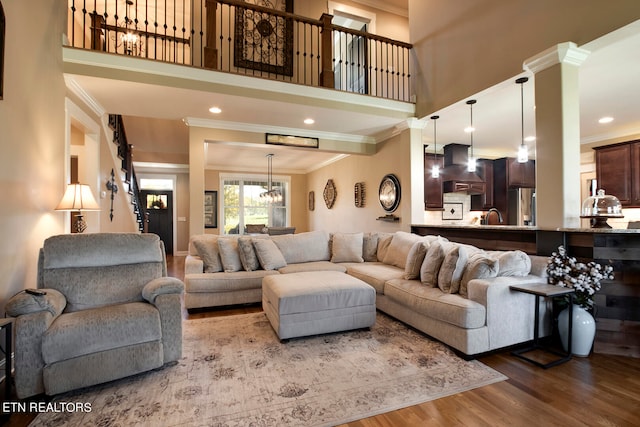 living room with a high ceiling, ornate columns, sink, ornamental molding, and hardwood / wood-style flooring