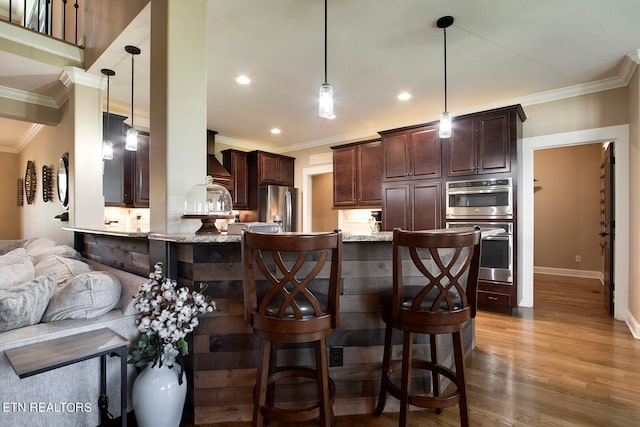 kitchen featuring light wood-type flooring, decorative light fixtures, stainless steel appliances, kitchen peninsula, and ornamental molding